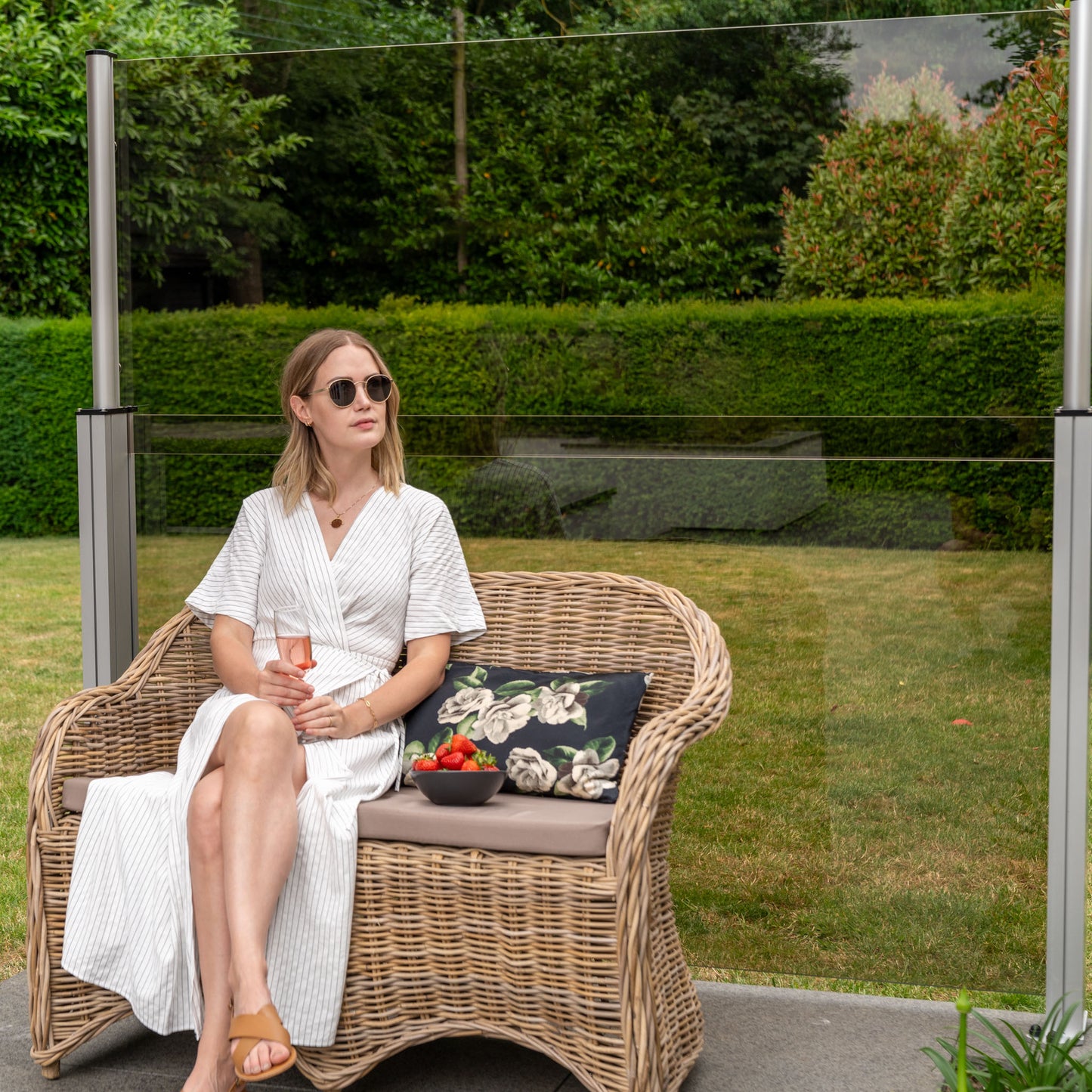 women sat on a wicker chair in front of a bronze glass balustrade on a patio