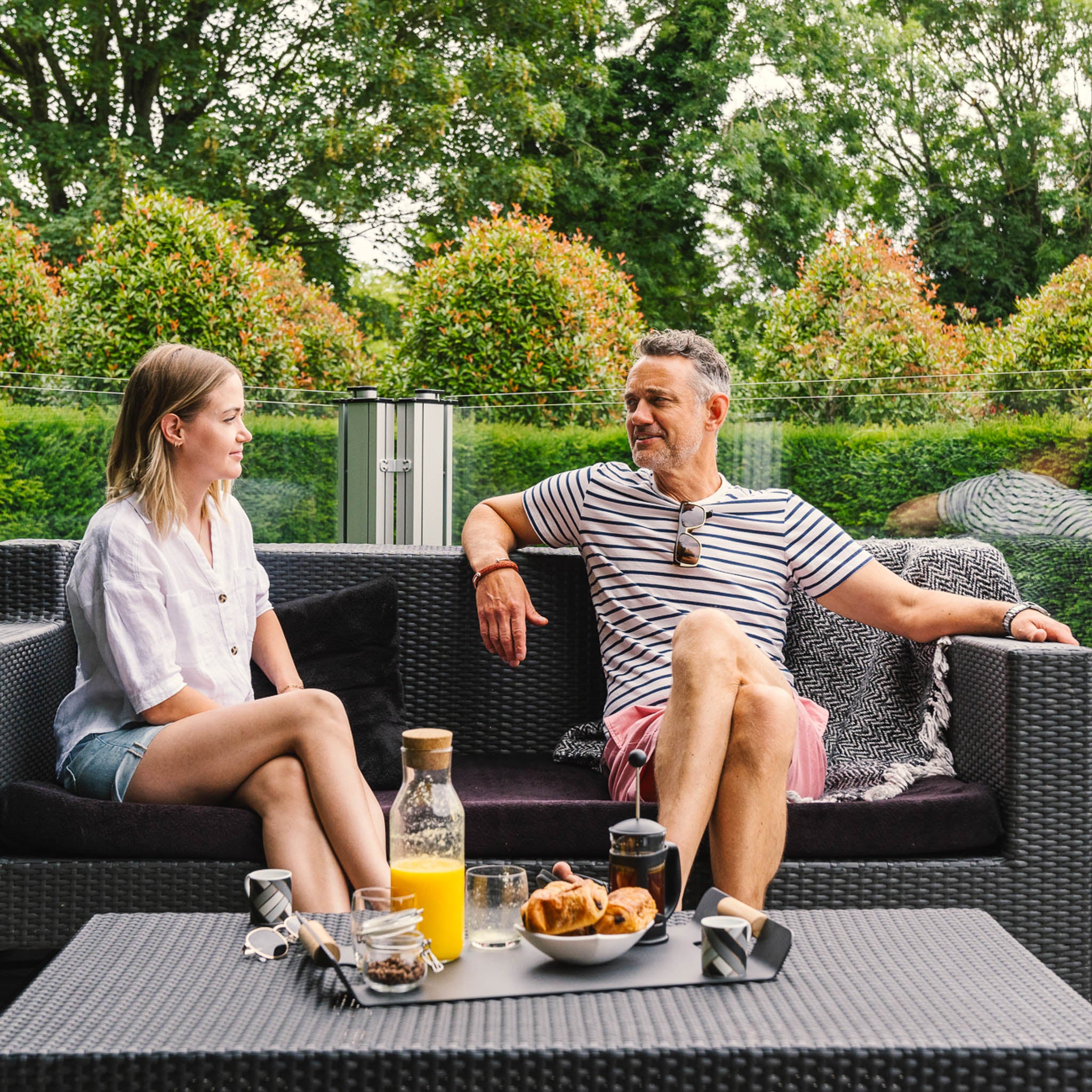 couple enjoying breakfast on a garden sofa with glass balustrades in the background