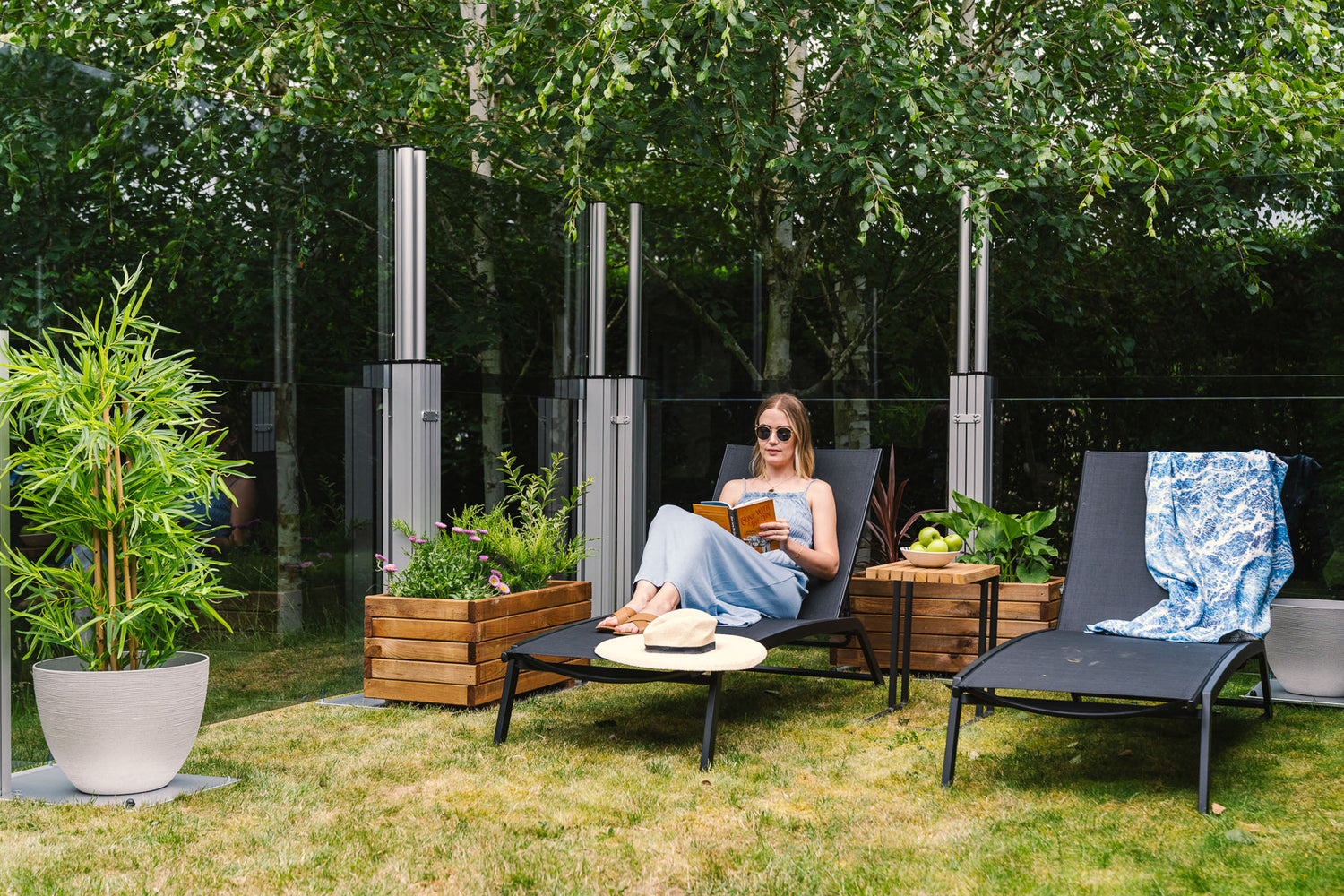 women reading a book on a sunlounge with glass windbreakers framing the green space
