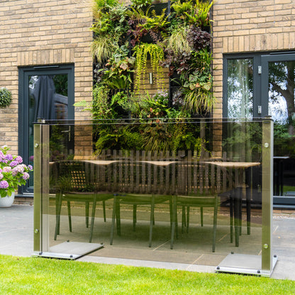 Bronze tinted glass panel with freestanding feet in front of a patio dining set