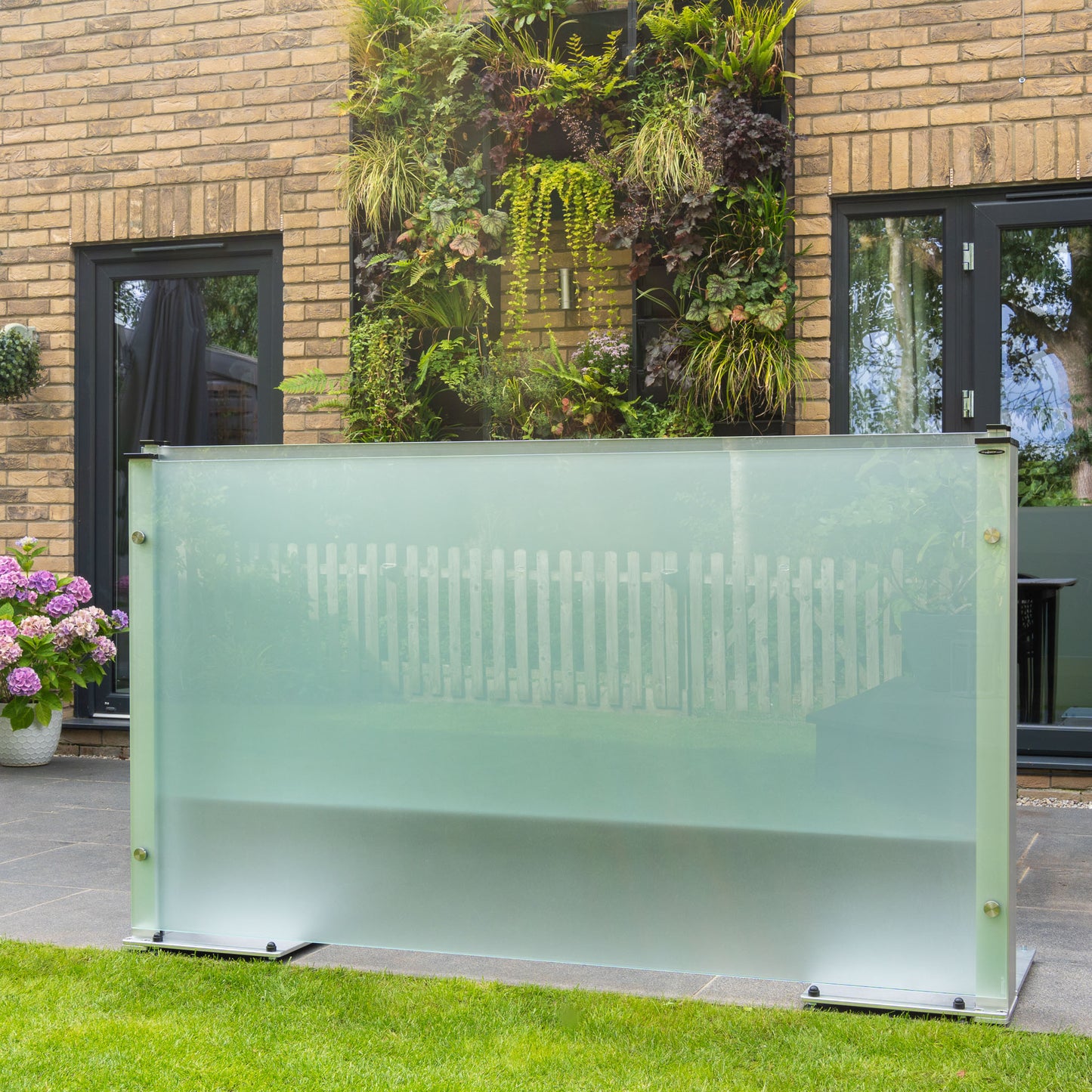 Retracted frosted glass screen with metal feet on a patio with grass border