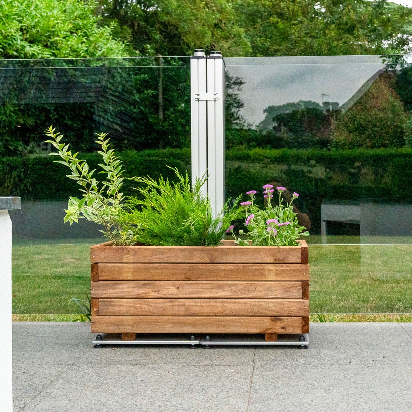 A wooden planter sat on the foot of a grey tinted glass windbreaker
