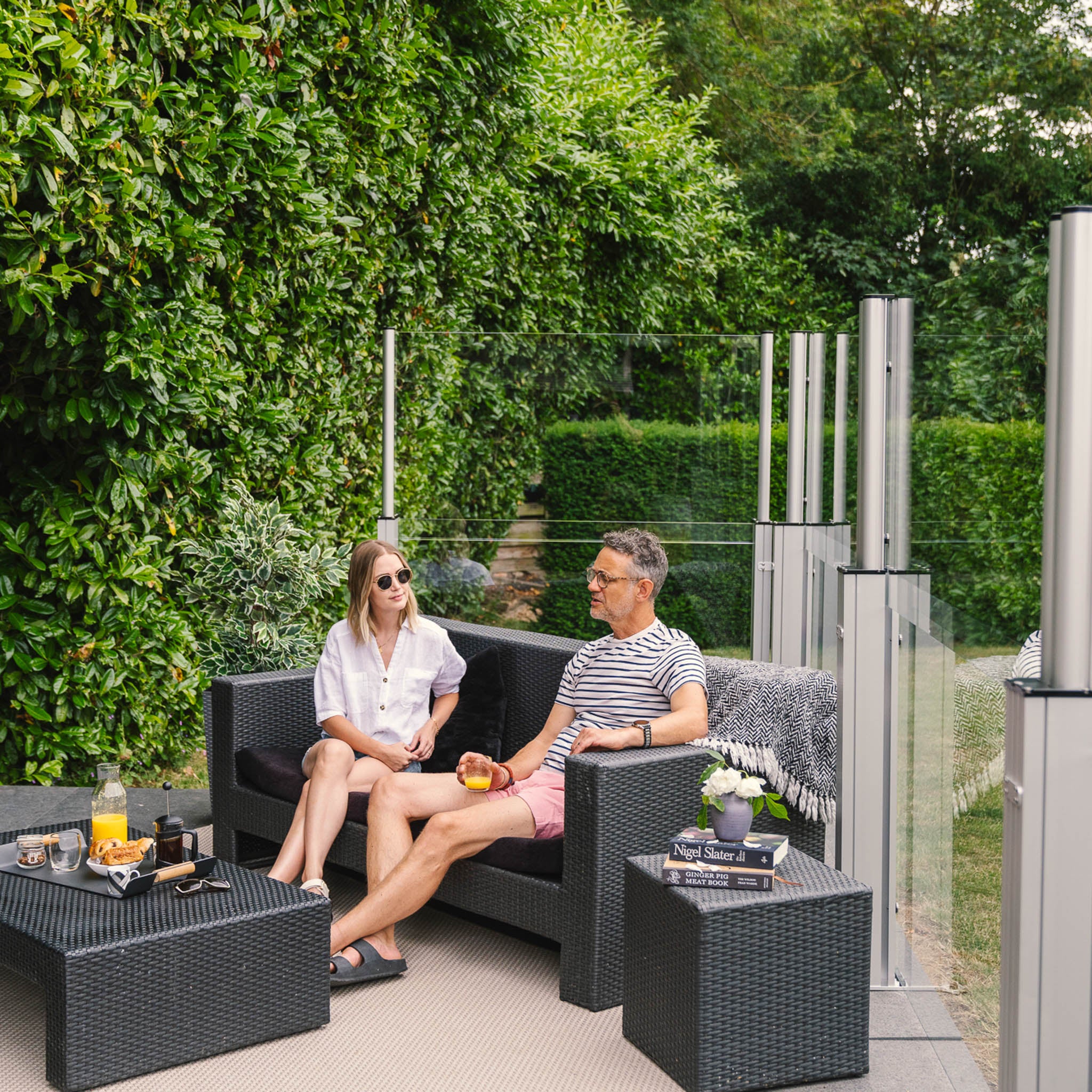 a couple enjoying breakfast on a patio sheltered by glass windbreakers